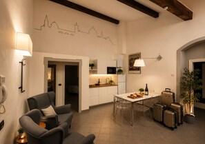 A modern living room with a sofa, a dining table with chairs, a kitchen area, and a staircase leading to another level. - Red Door Dream App. 3 (Firenze)