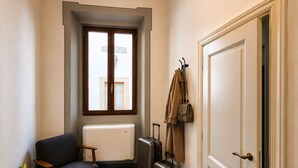 Ein Zimmer mit einer Couch, einem Heizkörper, einem Koffer und einem Kleiderständer mit einer Tasche.