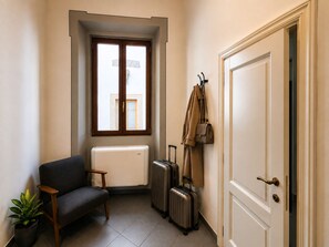 A room with a sofa, a radiator, a suitcase, and a coat rack with a bag. - Red Door Dream App. 3 (Firenze)
