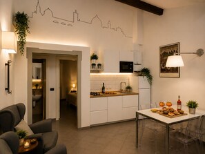 Eine moderne Küche mit weißen Schränken, ein Essbereich mit Tisch und Stühlen sowie ein Flur, der zum Schlafzimmer führt.