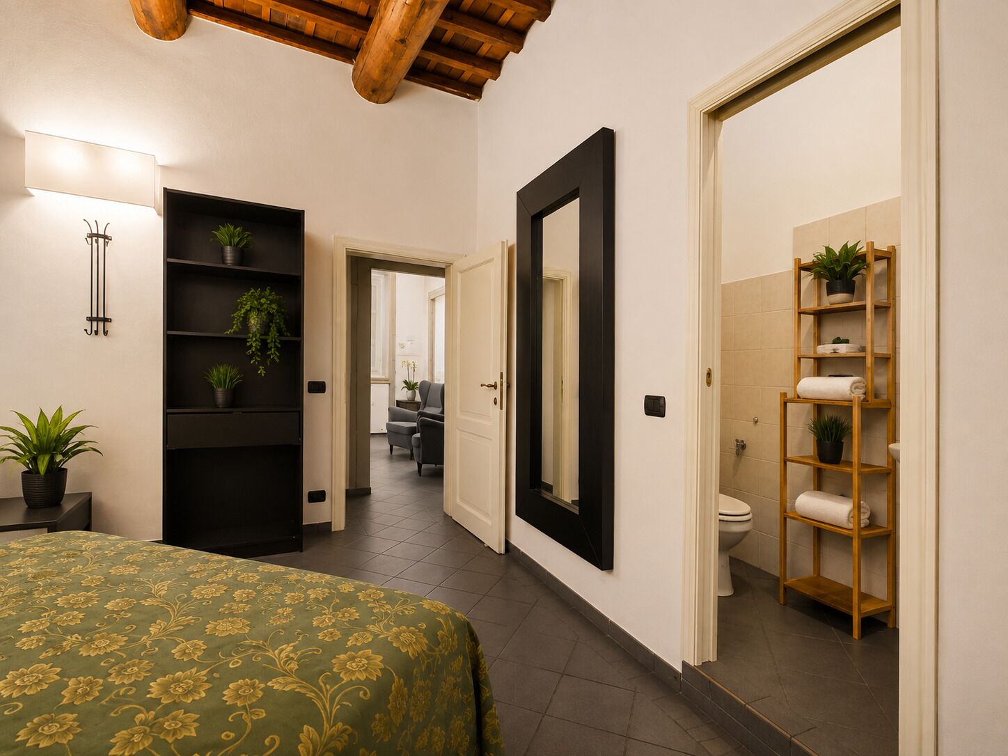 Une chambre d’hôtel comprenant un lit, un grand miroir, une armoire et une salle de bain avec des toilettes et des étagères.