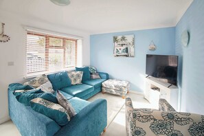 A living room with a sectional sofa, ottoman, TV stand, and artwork on the wall.