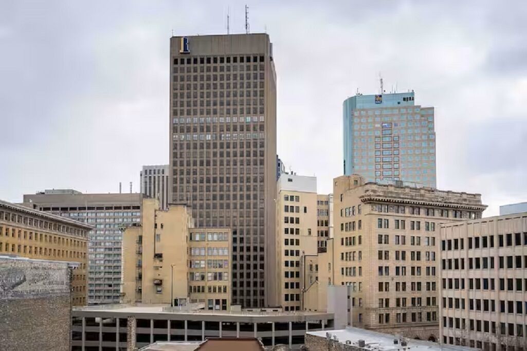 A cityscape with a prominent tall building, a shorter building with a blue facade, and a parking structure.