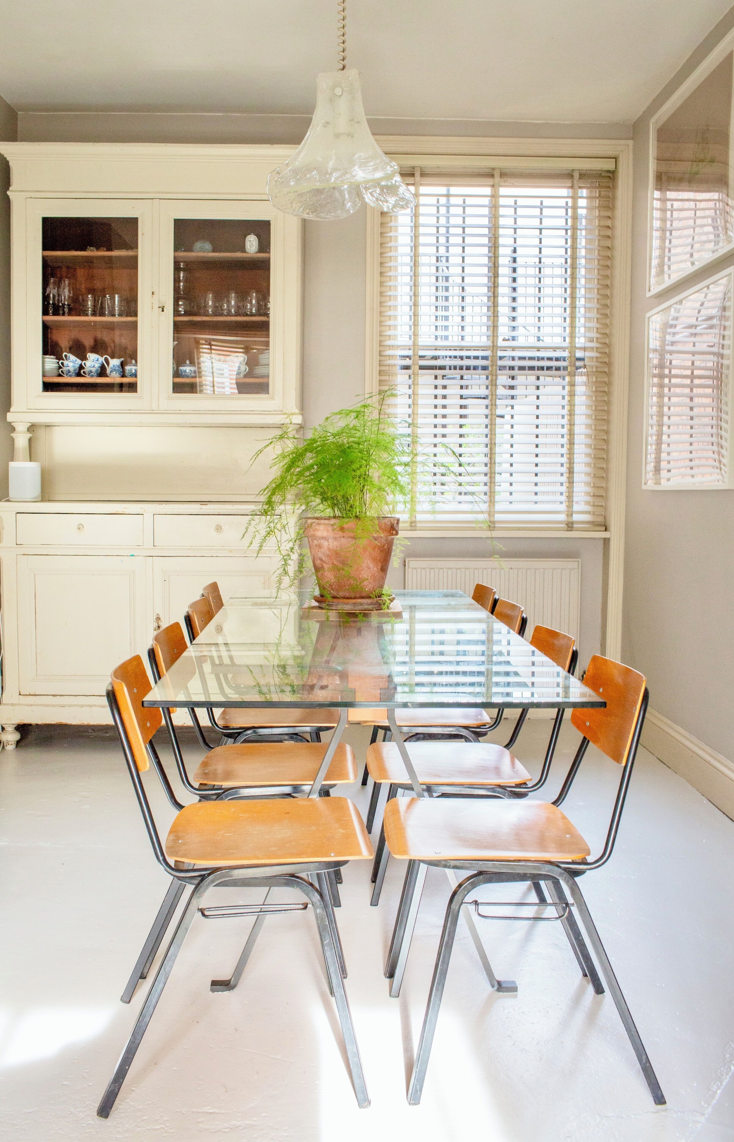 A dining area with a glass table, metal chairs, a potted plant, and a white cabinet with glass doors.