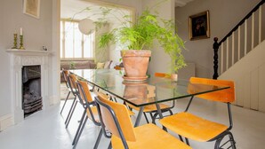 A dining area with a glass table, orange chairs, a potted plant, a fireplace, and a staircase. - Spacious 4-Bedroom Victorian Townhouse | Sleeps 8 | Central London (E1) (London)