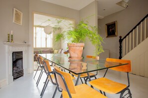 A dining area with a glass table, orange chairs, a potted plant, a fireplace, and a staircase. - Spacious 4-Bedroom Victorian Townhouse | Sleeps 8 | Central London (E1) (London)