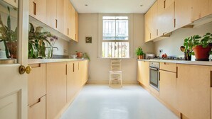 A kitchen with wooden cabinets, a white countertop, a window, and various potted plants. - Spacious 4-Bedroom Victorian Townhouse | Sleeps 8 | Central London (E1) (London)