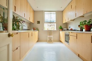 A kitchen with wooden cabinets, a white countertop, a window, and various potted plants. - Spacious 4-Bedroom Victorian Townhouse | Sleeps 8 | Central London (E1) (London)