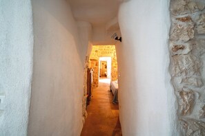 A narrow hallway with white walls and a stone wall on the right, leading to a room with a bed and a wooden wardrobe. - Torrette di Ostuni – Private Villa with Pool near Ostuni (Ostuni)