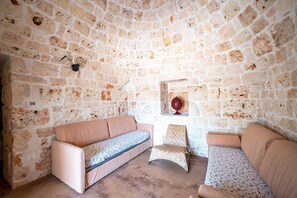 A stone-walled room with a sofa and a chair. - Torrette di Ostuni · Trullo with private pool in olive grove, dogs welcome (Ostuni)