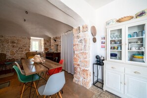A dining area with a stone wall, a wooden table, and colorful chairs. - Torrette di Ostuni · Trullo with private pool in olive grove, dogs welcome (Ostuni)