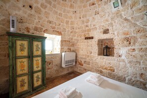 A stone-walled room with a bed, a cabinet with floral designs, an air conditioning unit, and a small shelf with a lantern. - Torrette di Ostuni – Private Villa with Pool near Ostuni (Ostuni)