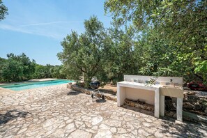 A stone patio with a pool, outdoor grill, and a seating area with a tiled table. - Torrette di Ostuni – Private Villa with Pool near Ostuni (Ostuni)