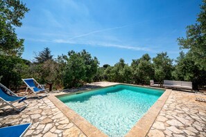 A rectangular swimming pool with clear blue water, surrounded by stone tiles and shaded by trees. - Torrette di Ostuni · Trullo with private pool in olive grove, dogs welcome (Ostuni)
