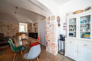 A stone-walled room with a wooden dining table, chairs, and a white cabinet with glassware. - Torrette di Ostuni – Private Villa with Pool near Ostuni (Ostuni)