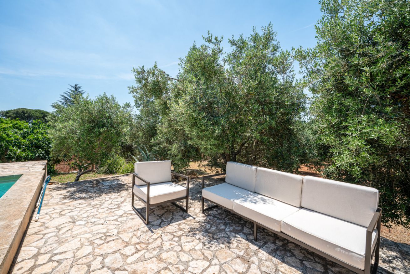 An outdoor seating area with a stone floor, two white cushioned chairs, and a sofa.