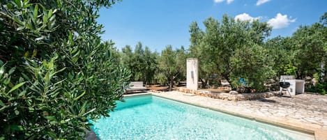 Piscina límpida rodeada por oliveiras e um terraço de pedra.