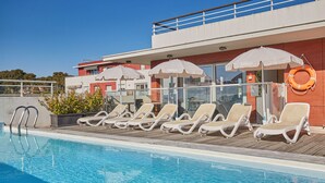 Ein Schwimmbecken mit Liegestühlen und Sonnenschirmen, einem Rettungsring sowie ein Gebäude mit Balkon.