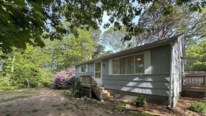 A single-story house with a front porch, a small deck, and a garden with flowering plants.