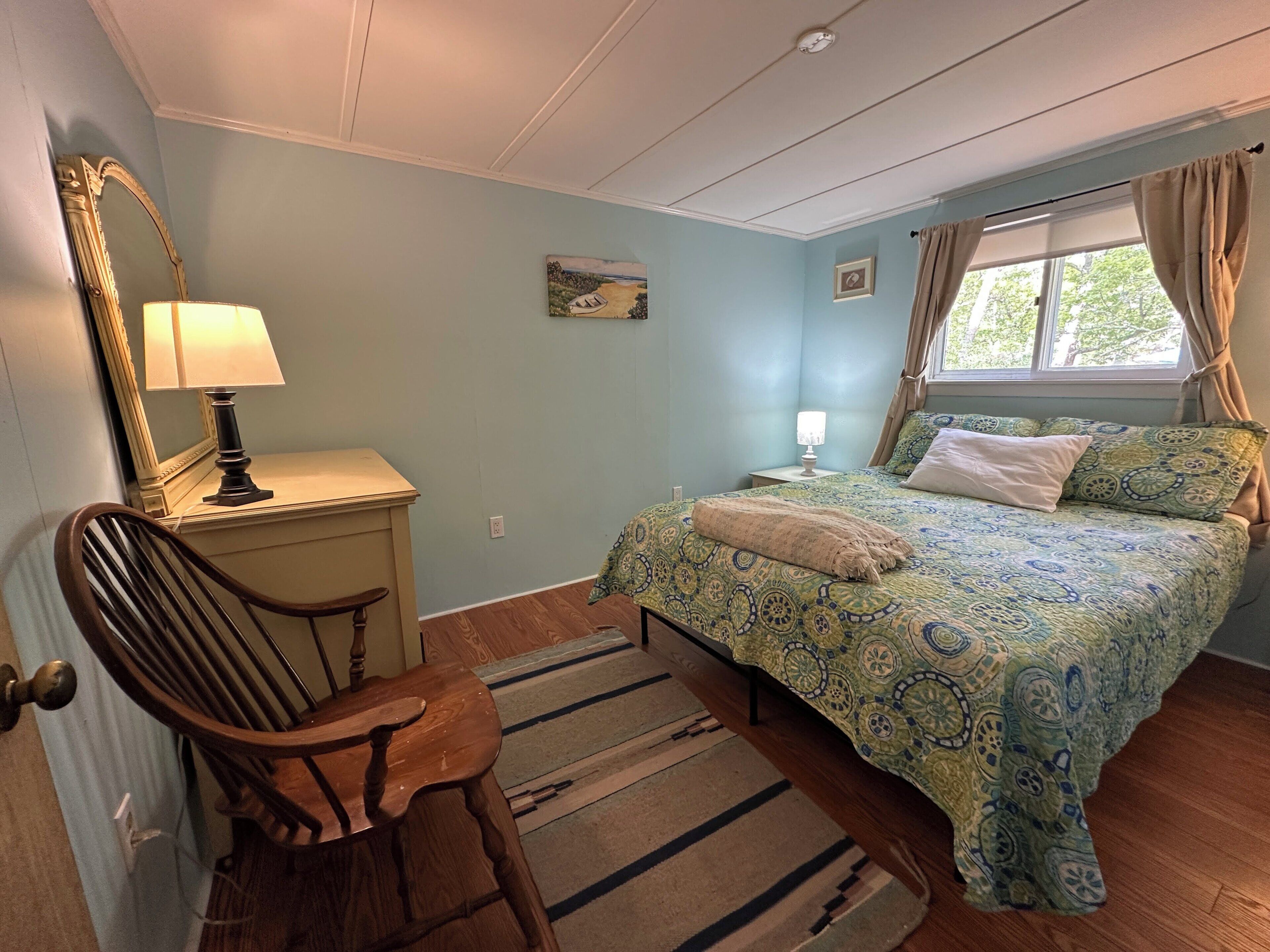 A bedroom with a bed, a chair, a lamp, a rug, and a window with curtains.