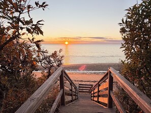 A wooden staircase leading to a beach with a sunset in the background. - Driftwood Cottages - 85 - Lobster (Eastham)