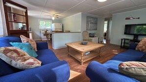 Una sala de estar con sofás azules, una mesa de centro de madera, una zona de cocina con estufa y un televisor.