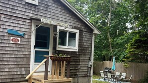A wooden house with a porch, a small deck, and a fenced backyard with a grill and patio furniture.