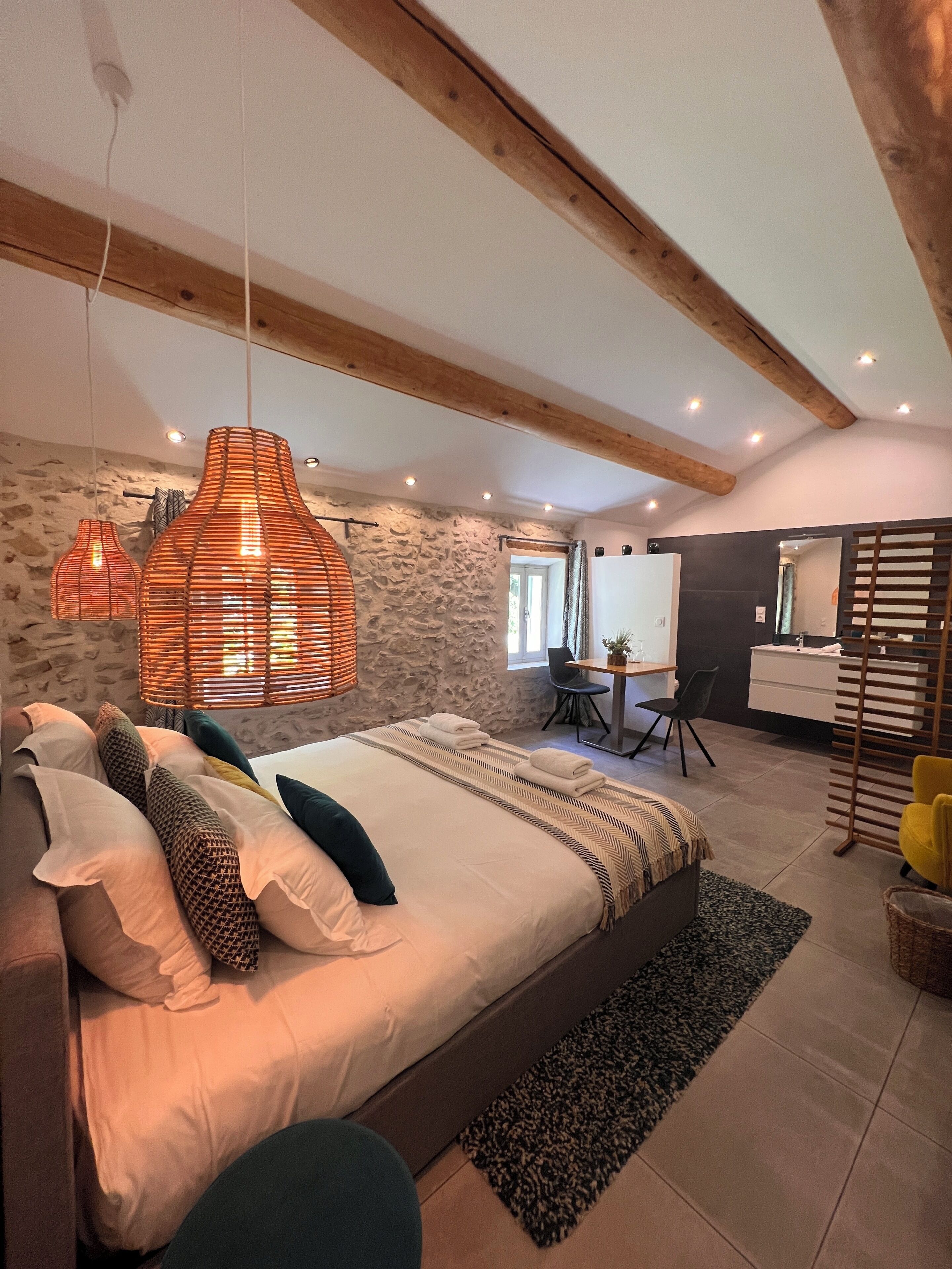 Une chambre à coucher avec un grand lit, un mur en pierre, un plafond en bois et une salle de bain avec un miroir et un lavabo.