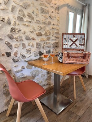 Een stenen wand binnen met een houten tafel gedekt voor twee personen, twee rode stoelen en een rieten mand met bestek.