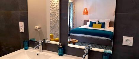A bathroom with two sinks, a mirror, and a bed visible in the reflection.