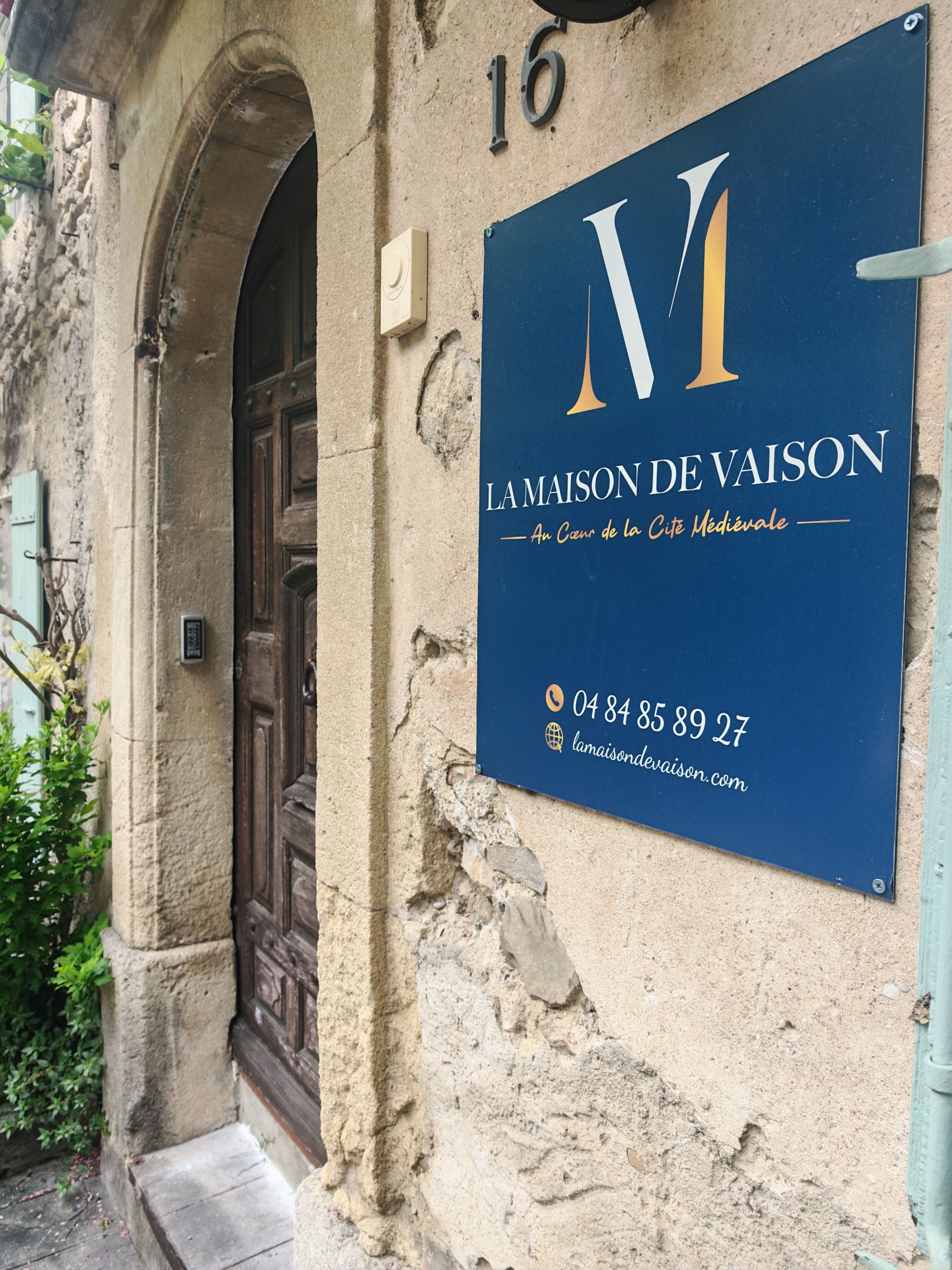 A sign for 'La Maison de Vaison' with a medieval theme, including a phone number and website.