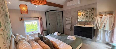 A modern bedroom with a large bed, a shower, a vanity with a mirror, and a window with a view.