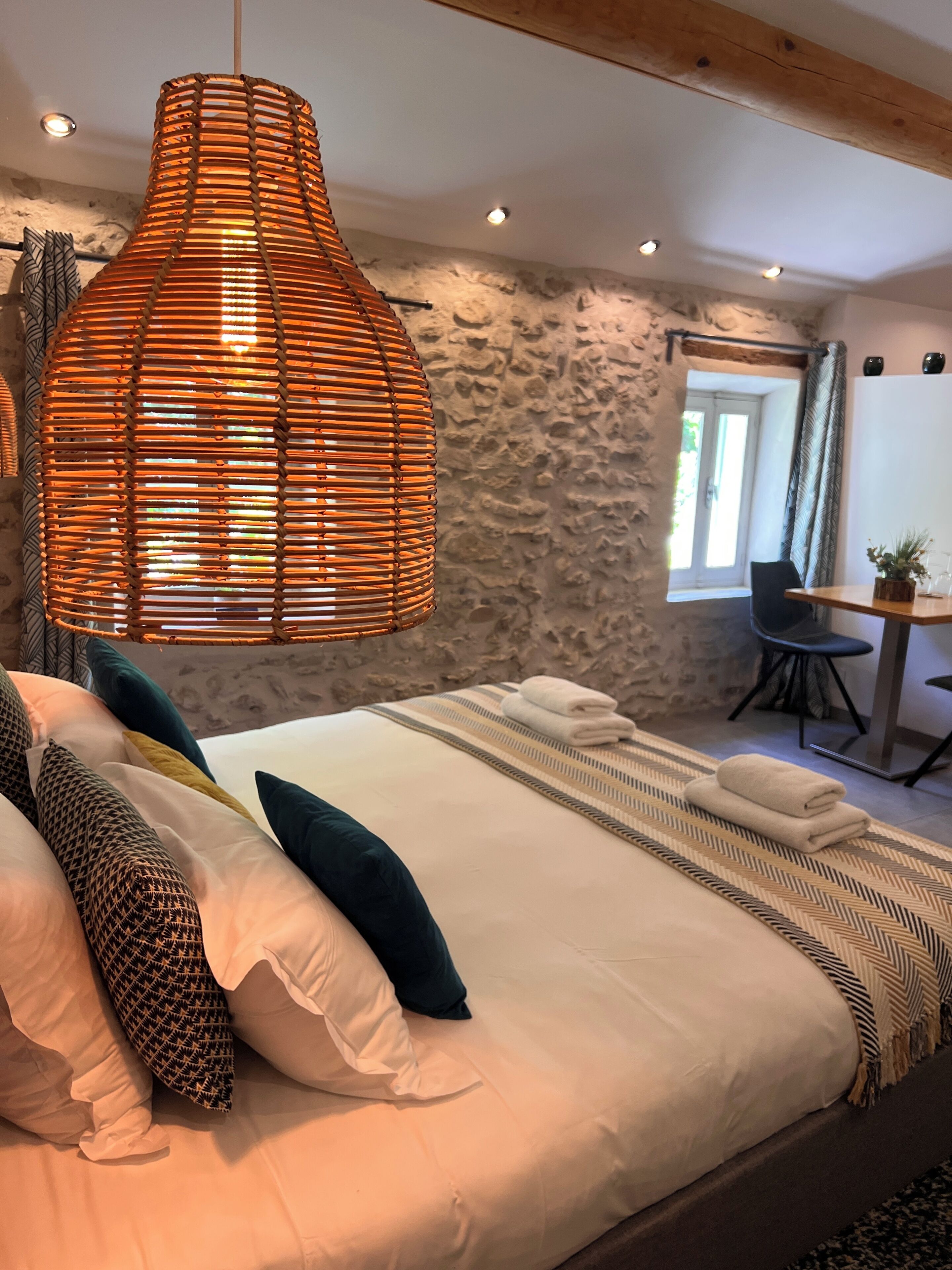 A bedroom with a large bed, a hanging light fixture, a stone wall, a desk, and a chair.