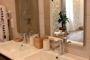 Een badkamer met een grote spiegel, twee wastafels, een douche en een plant in pot.
