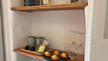 A shelf with a framed sign, a diffuser, and a QR code. Below, there are teapots, a tray with pastries, and a kettle.