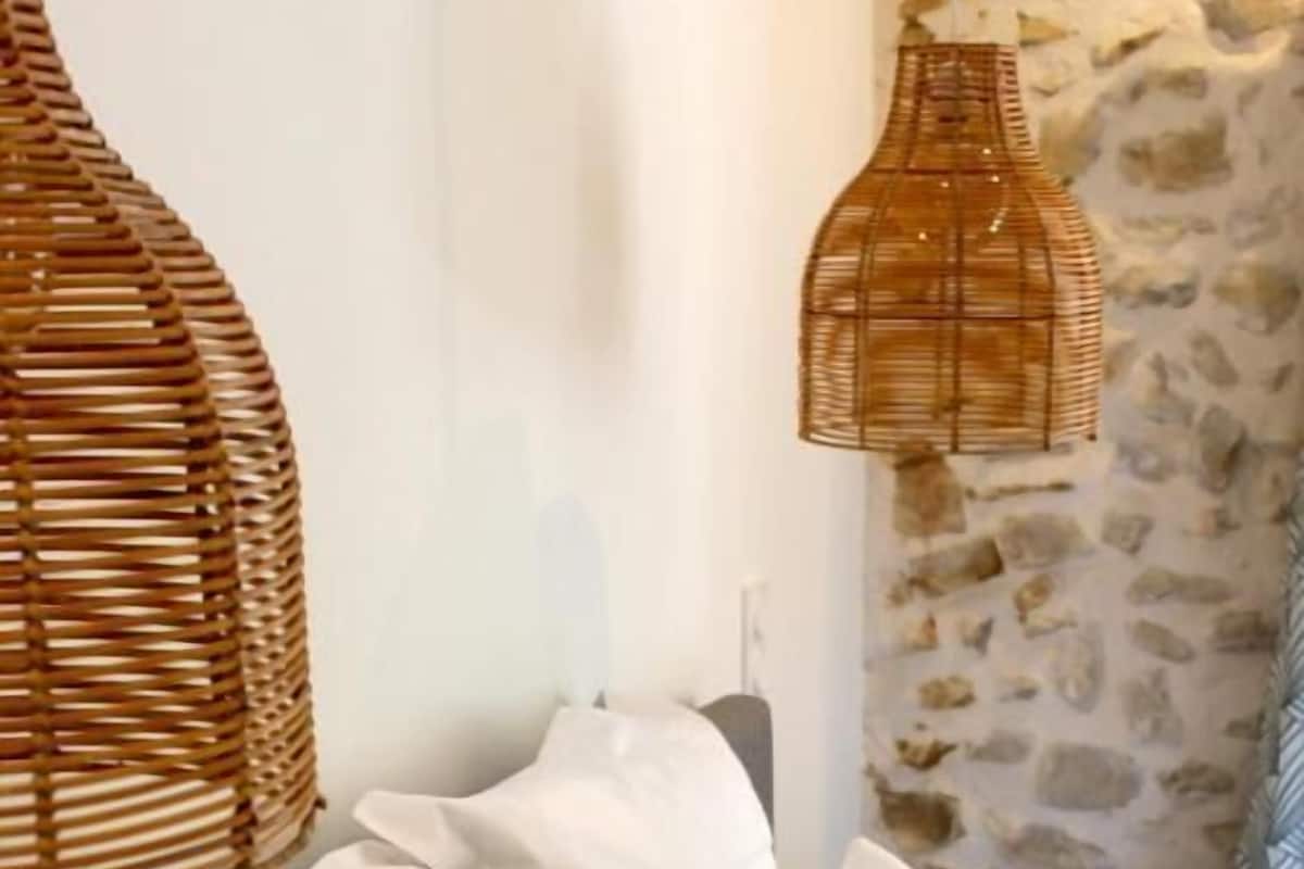 Ein Bett mit weißen und türkisblauen Kissen, einem Korbhaupt und einer Steinwand.