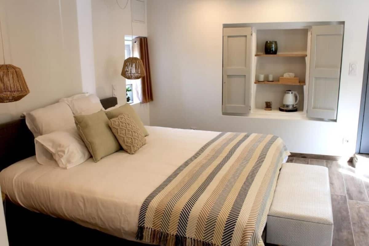 Ein Schlafzimmer mit einem Bett, Nachttischen, einer eingebauten Ablage mit Gegenständen und einer Pendelleuchte.