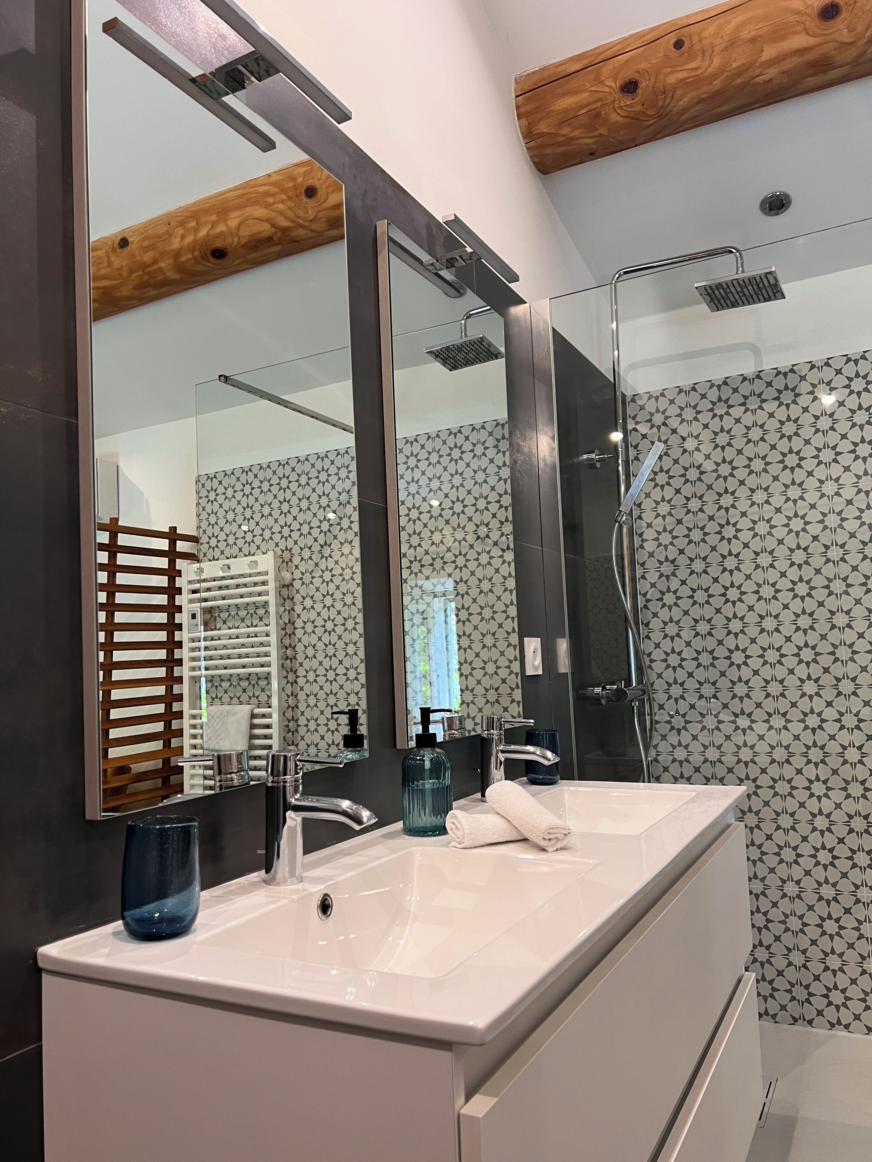 Une salle de bain moderne avec un grand miroir, un meuble-lavabo blanc, une douche et des carreaux décorés.