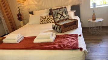 Una cama bien hecha con sábanas blancas, una manta roja y una maleta de mimbre sobre la cama.