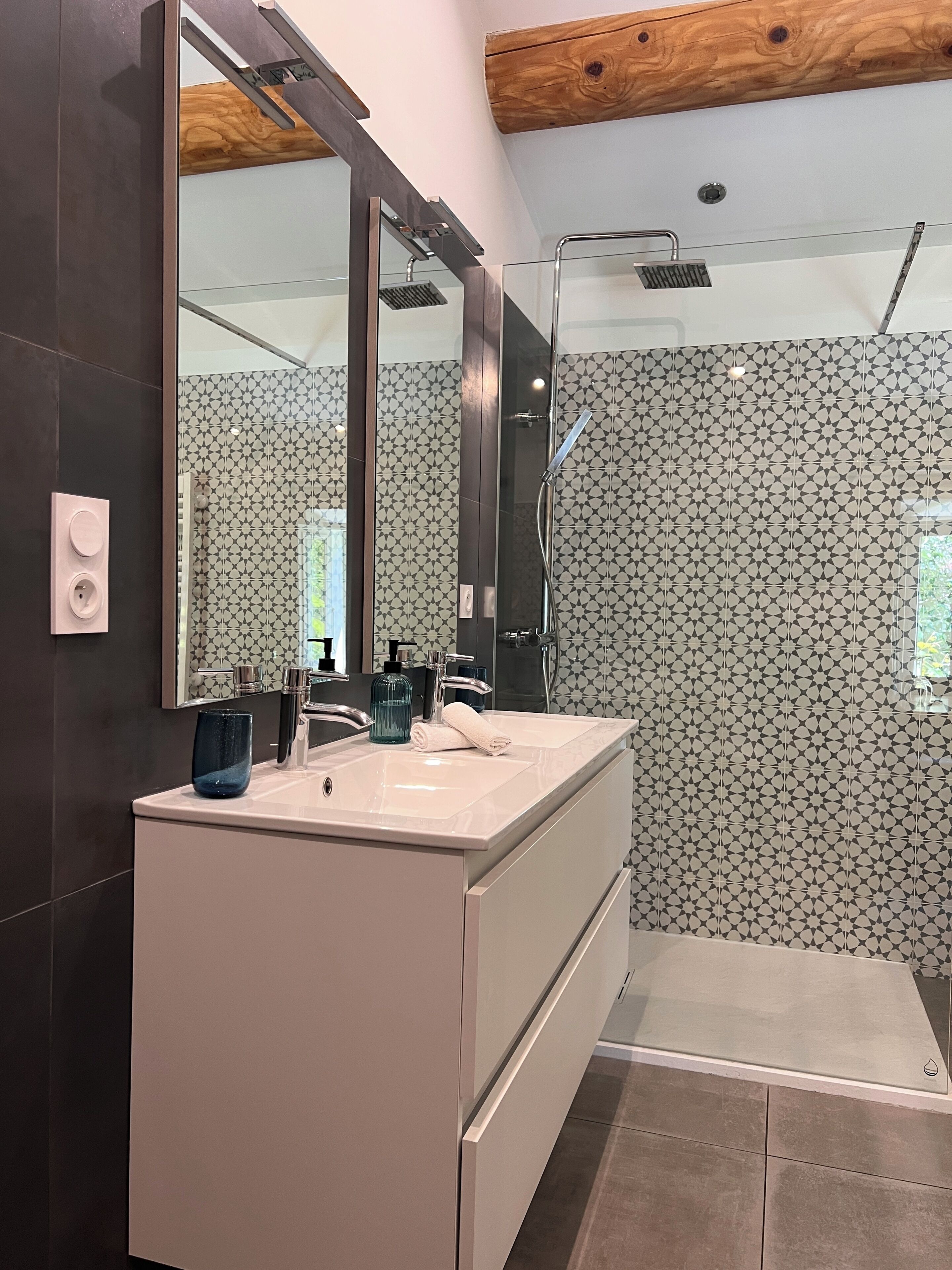 A modern bathroom with a large mirror, a glass shower enclosure, and patterned tiles.