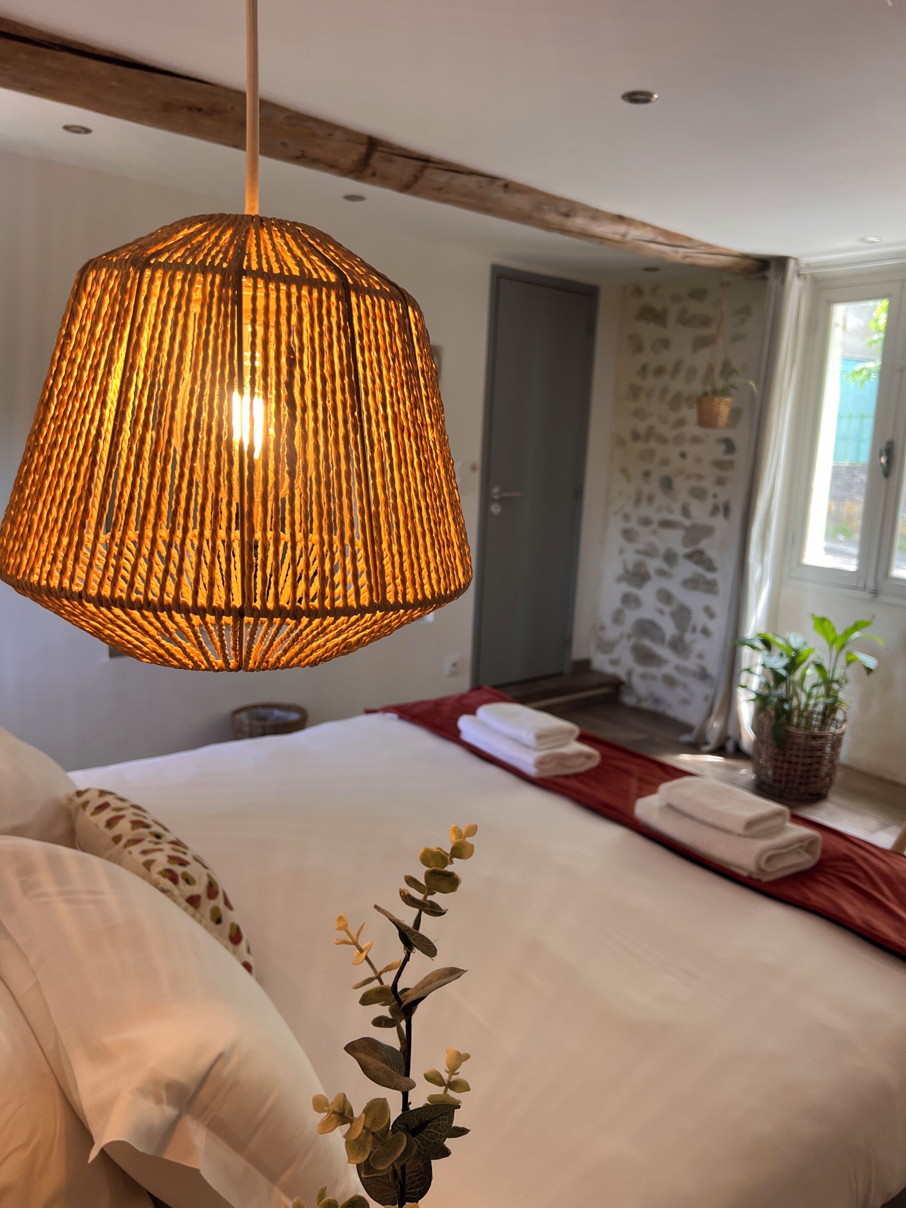 A bedroom with a large bed, a hanging lamp, and a potted plant.