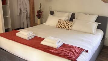 Una cama bien hecha con ropa de cama blanca y roja, un cabecero gris y suelo de madera.