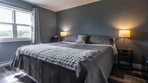 A bedroom with a large bed, two bedside tables with lamps, a window with curtains, and a view of the outdoors.