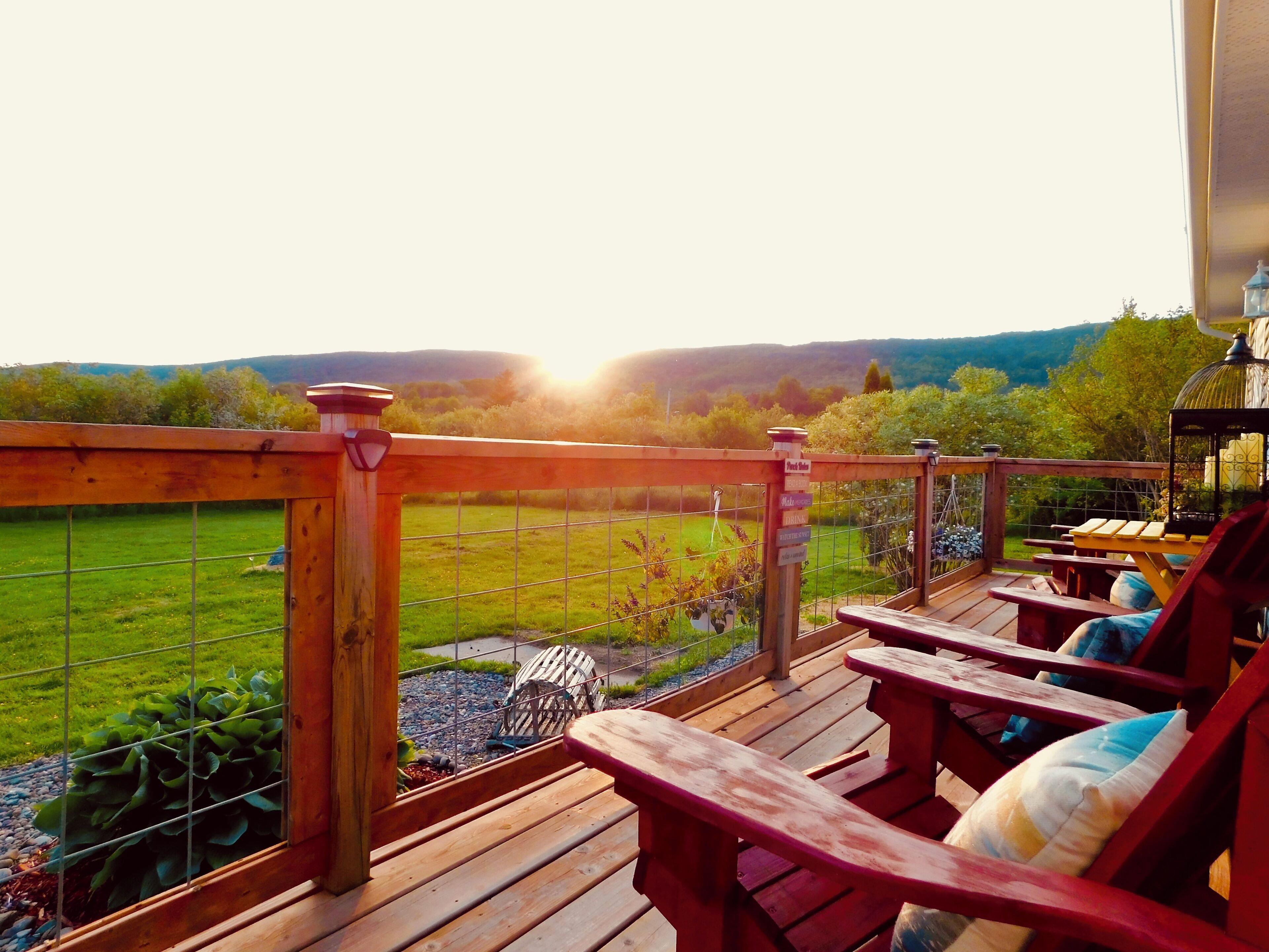 A wooden deck with a view of a green field and hills.