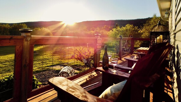 A wooden deck with a view of a field and hills, a bottle of wine, and a lantern.