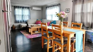 A living room with a sofa, wooden dining table, chairs, and a vase with flowers.