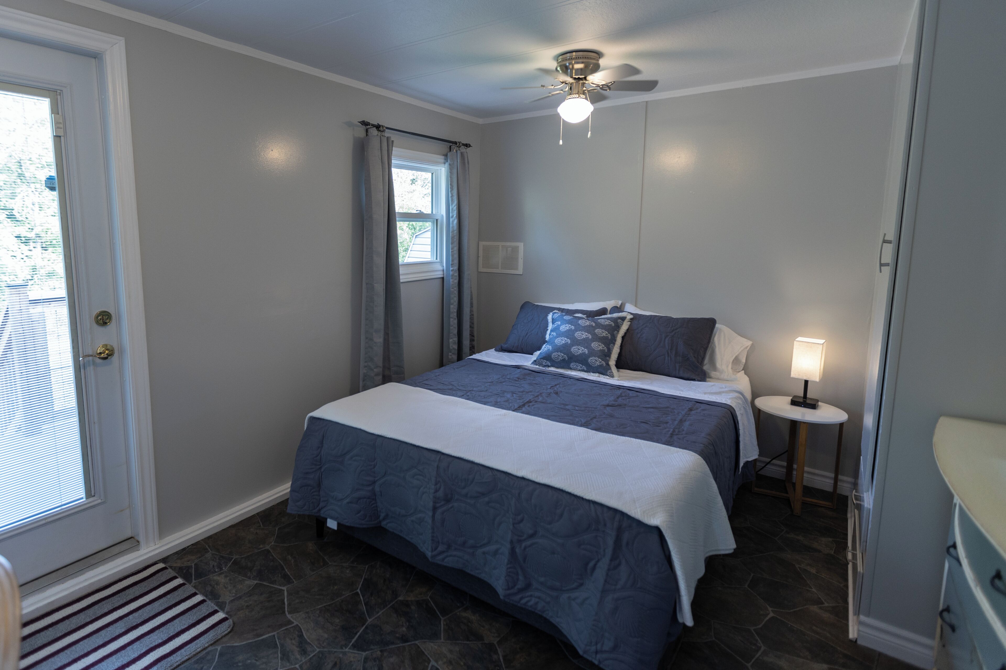 Une chambre à coucher avec un lit, une table de chevet, une lampe, un ventilateur de plafond et une porte.
