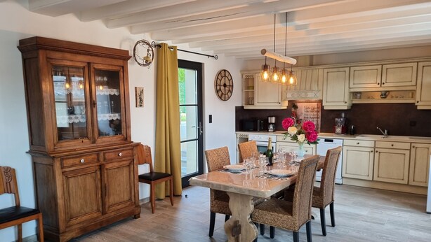 A dining area with a wooden table set for six, surrounded by wicker chairs, a wooden cabinet, and a kitchen in the background. - Cosy house "La Petite Cigogne" in Baie de Somme. (Boismont)