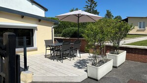 A patio with a table and chairs, a large umbrella, and planters with small trees. - Cosy house "La Petite Cigogne" in Baie de Somme. (Boismont)