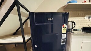 Ein kompakter, schwarzer Kühlschrank mit Energiestick, eine Metallschüssel auf einer Ablagefläche und ein Wasserkocher auf der Arbeitsplatte.